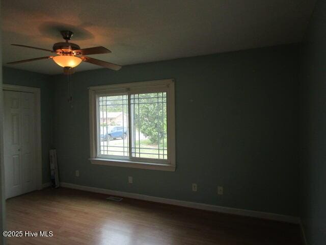 spare room featuring wood finished floors, ceiling fan, baseboards, and visible vents