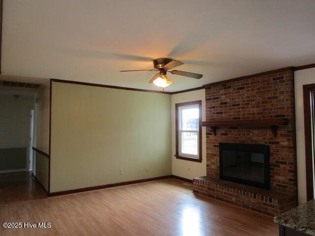 unfurnished living room with a brick fireplace, light wood-type flooring, and ornamental molding