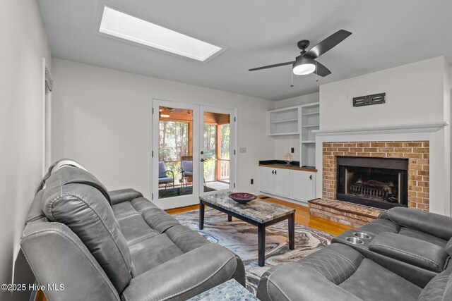 living area with ceiling fan, a textured ceiling, french doors, light wood-type flooring, and a skylight