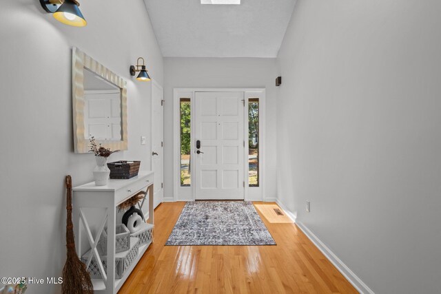 foyer with a fireplace, ceiling fan, baseboards, and light wood-style floors