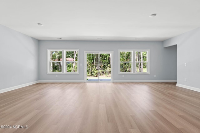 unfurnished living room featuring light wood-type flooring, baseboards, and plenty of natural light