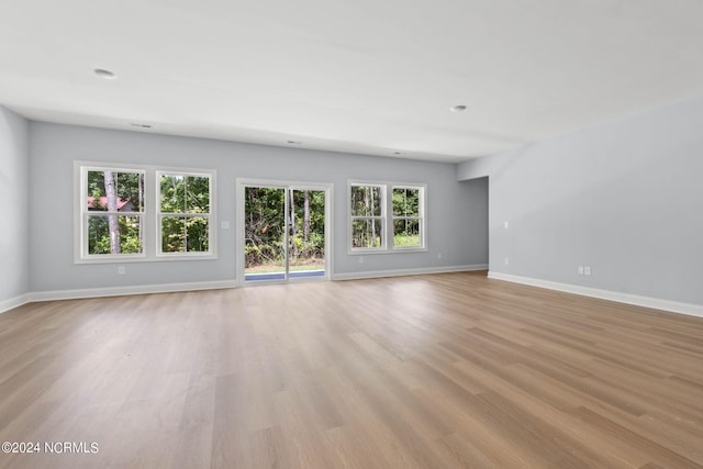 unfurnished living room featuring a wealth of natural light, light wood-style floors, and baseboards