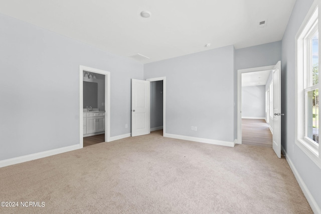 unfurnished bedroom with light colored carpet, baseboards, and connected bathroom
