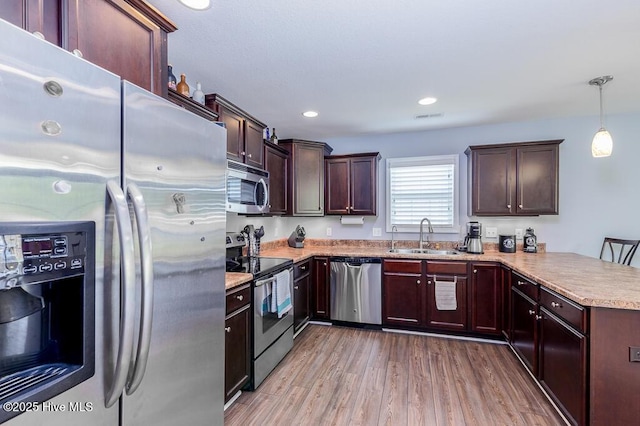 kitchen featuring wood finished floors, a sink, light countertops, a peninsula, and stainless steel appliances