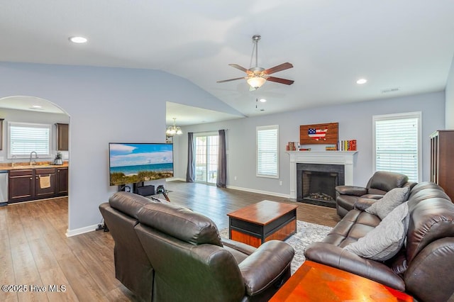 living area with vaulted ceiling, wood finished floors, ceiling fan with notable chandelier, and a fireplace