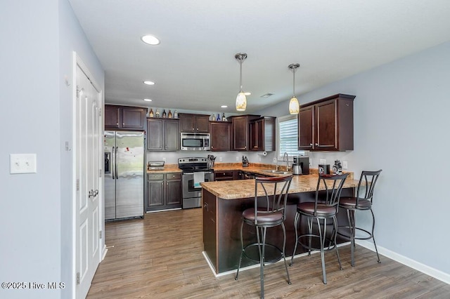 kitchen with dark brown cabinetry, appliances with stainless steel finishes, a breakfast bar, a sink, and a peninsula