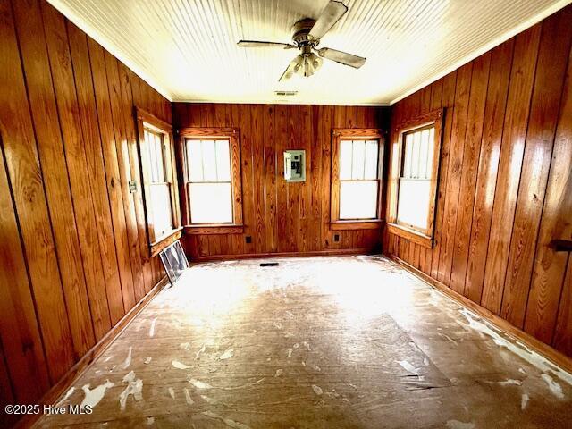 empty room featuring electric panel, plenty of natural light, wooden walls, and ceiling fan