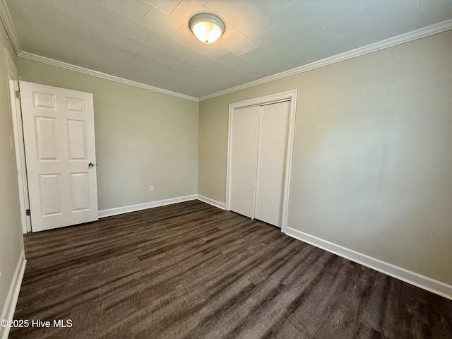 unfurnished bedroom with a closet, dark wood-style flooring, baseboards, and ornamental molding