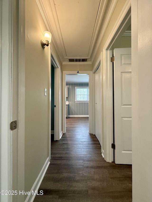 corridor featuring dark wood finished floors, ornamental molding, visible vents, attic access, and baseboards