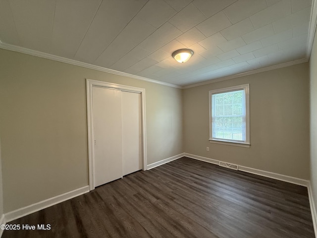unfurnished bedroom featuring baseboards, ornamental molding, a closet, dark wood-style floors, and visible vents