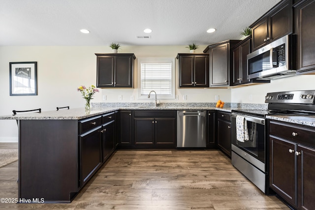 kitchen with visible vents, appliances with stainless steel finishes, a peninsula, wood finished floors, and light stone countertops