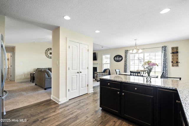 kitchen with dark cabinetry, open floor plan, an inviting chandelier, and dark wood-type flooring