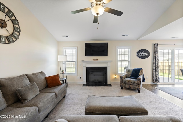 living room featuring lofted ceiling, baseboards, a fireplace with flush hearth, visible vents, and ceiling fan