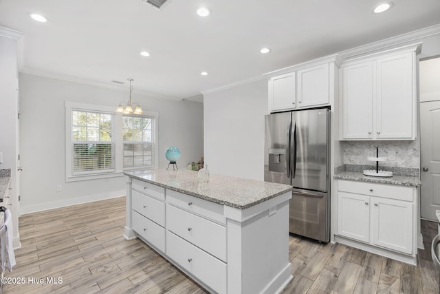 kitchen featuring crown molding, stainless steel refrigerator with ice dispenser, a kitchen island, and white cabinetry