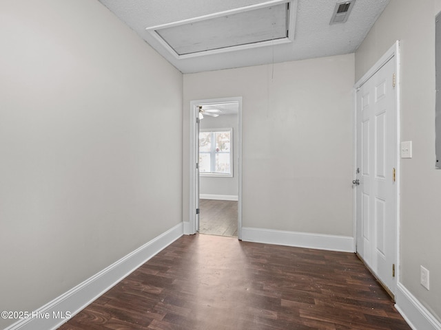 unfurnished room with visible vents, baseboards, attic access, dark wood-type flooring, and a textured ceiling