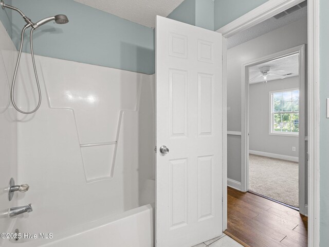 full bath featuring a textured ceiling, visible vents, bathing tub / shower combination, and wood finished floors
