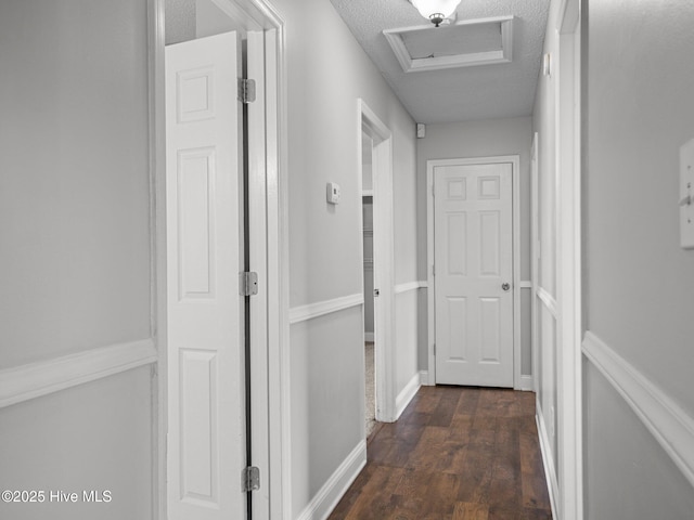 corridor with baseboards, attic access, dark wood-style flooring, and a textured ceiling
