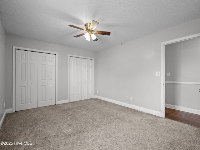 unfurnished bedroom with carpet floors, a textured ceiling, two closets, a ceiling fan, and baseboards