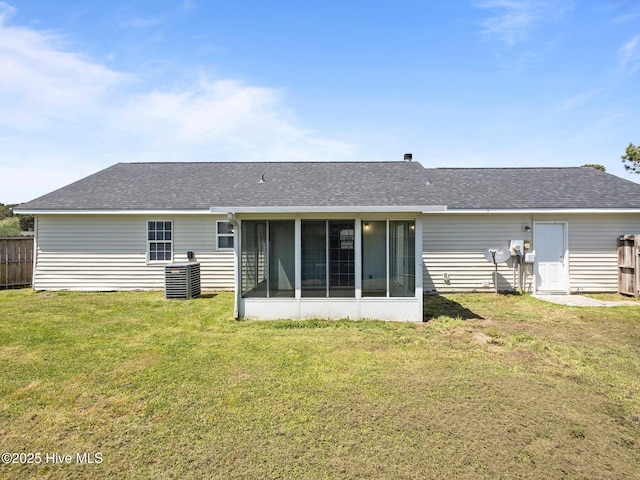 rear view of house featuring a lawn, fence, a shingled roof, and a sunroom