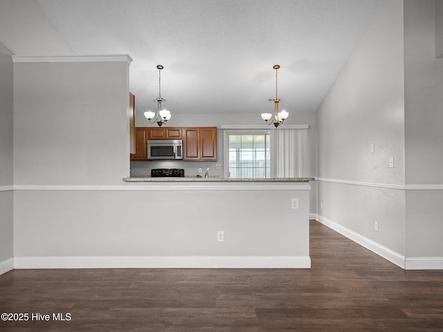 kitchen featuring an inviting chandelier, stainless steel microwave, brown cabinets, and dark wood finished floors