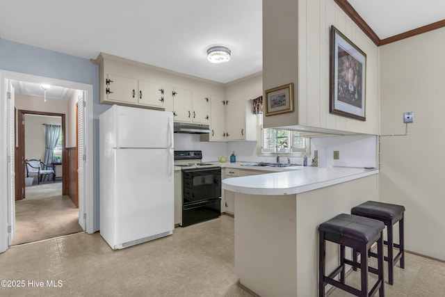kitchen with a peninsula, light countertops, freestanding refrigerator, under cabinet range hood, and electric stove