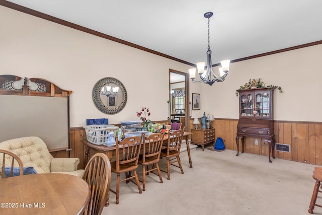 carpeted dining space featuring wooden walls, a notable chandelier, ornamental molding, and wainscoting