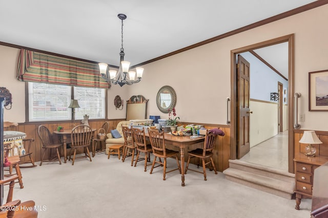 dining space with an inviting chandelier, ornamental molding, wooden walls, carpet flooring, and wainscoting