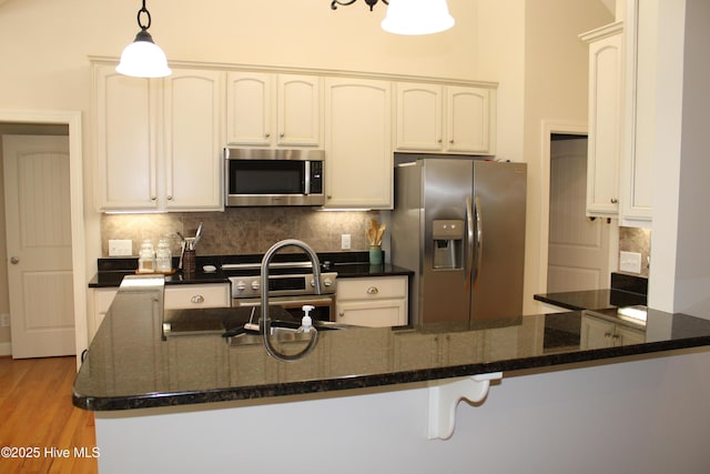 kitchen featuring dark stone counters, tasteful backsplash, hanging light fixtures, a sink, and stainless steel appliances