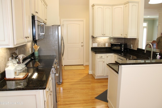 kitchen with dark stone counters, decorative backsplash, light wood-type flooring, a peninsula, and appliances with stainless steel finishes