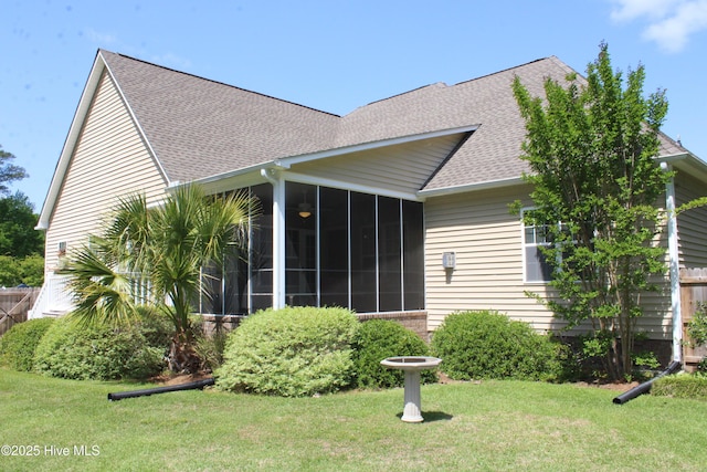 back of property with a sunroom, a lawn, and roof with shingles