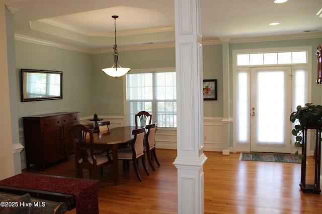 dining area with light wood-style floors, a wainscoted wall, ornate columns, and crown molding