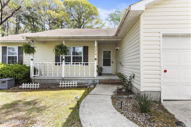 entrance to property featuring a yard, an attached garage, a shingled roof, and covered porch