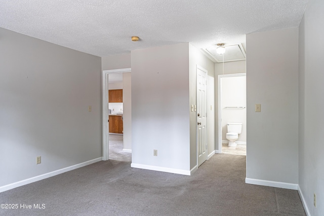 unfurnished bedroom with a textured ceiling, attic access, baseboards, and carpet