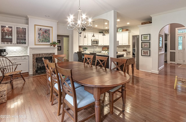 dining room featuring arched walkways, wood-type flooring, crown molding, a fireplace, and a chandelier