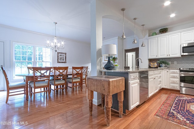 kitchen with stainless steel appliances, ornamental molding, light wood-style flooring, light stone counters, and a peninsula