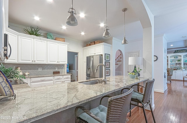kitchen with a sink, stainless steel appliances, light stone countertops, a kitchen breakfast bar, and crown molding