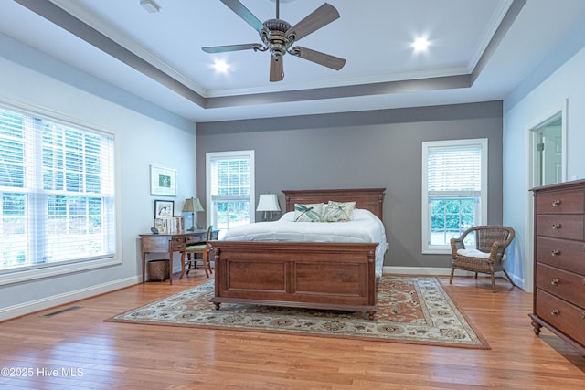 bedroom with ornamental molding, a raised ceiling, light wood-style floors, and baseboards