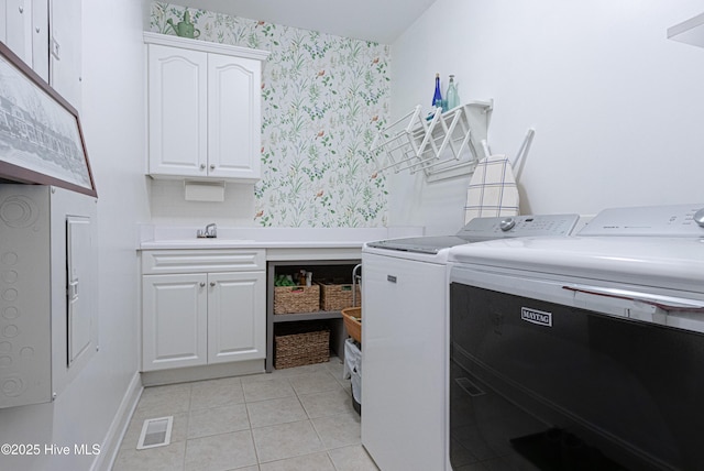 laundry room featuring wallpapered walls, washer and clothes dryer, cabinet space, light tile patterned flooring, and baseboards