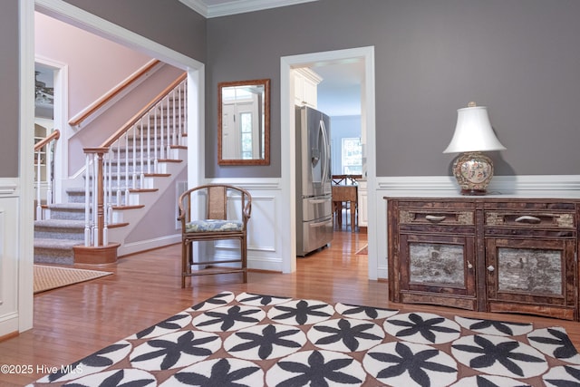living area with light wood-type flooring, stairway, ornamental molding, a wainscoted wall, and a decorative wall