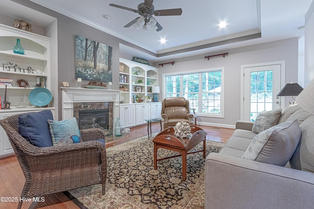 living area featuring ceiling fan, wood finished floors, crown molding, a high end fireplace, and built in features