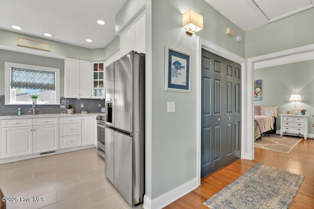 334 NE 48th St, Oak Island, NC 28465 - kitchen featuring appliances with stainless steel finishes, white cabinetry, glass insert cabinets, backsplash, and baseboards