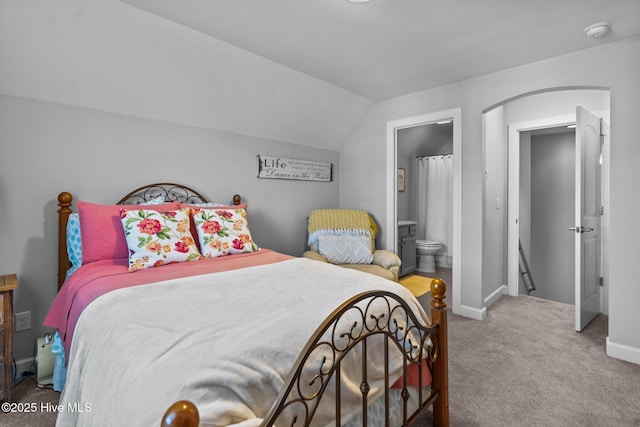 carpeted bedroom featuring arched walkways, lofted ceiling, baseboards, and ensuite bathroom