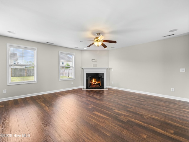 unfurnished living room with ceiling fan, dark wood-type flooring, a fireplace with flush hearth, visible vents, and baseboards