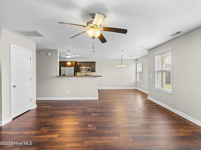 unfurnished living room with ceiling fan with notable chandelier, baseboards, dark wood-style floors, and visible vents