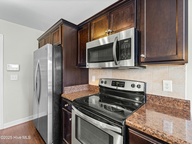 kitchen with dark stone counters, dark wood finished floors, dark brown cabinetry, stainless steel appliances, and backsplash