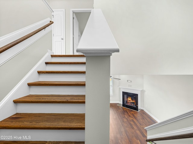 stairs with a glass covered fireplace, baseboards, and wood finished floors