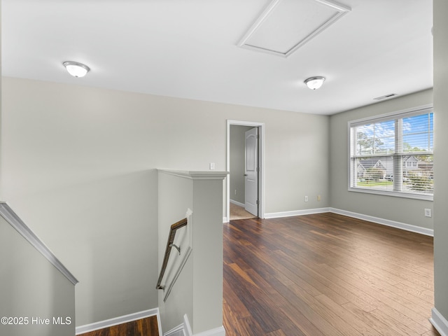 empty room featuring visible vents, baseboards, attic access, and dark wood finished floors