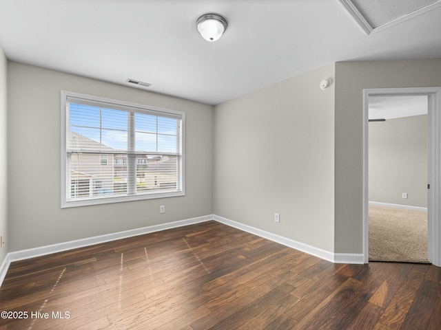 spare room featuring dark wood-type flooring, visible vents, and baseboards