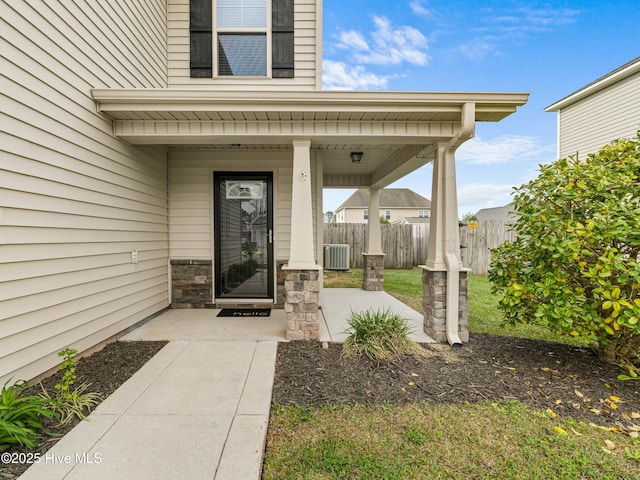 doorway to property with cooling unit, stone siding, and fence