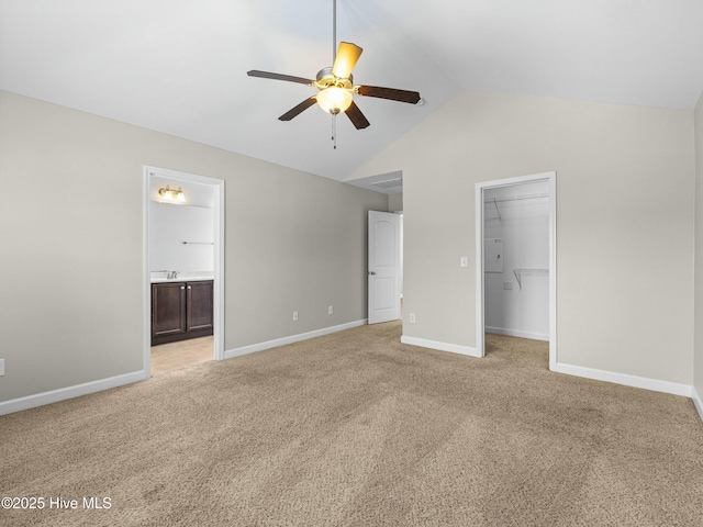 unfurnished bedroom featuring baseboards, vaulted ceiling, a closet, light carpet, and a walk in closet